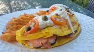 Close-up of a ham and egg omelette with vegetables and fries on a white plate.