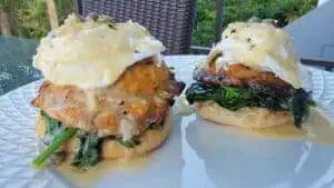 Two gourmet chicken sandwiches with spinach and egg on a white plate outdoors.