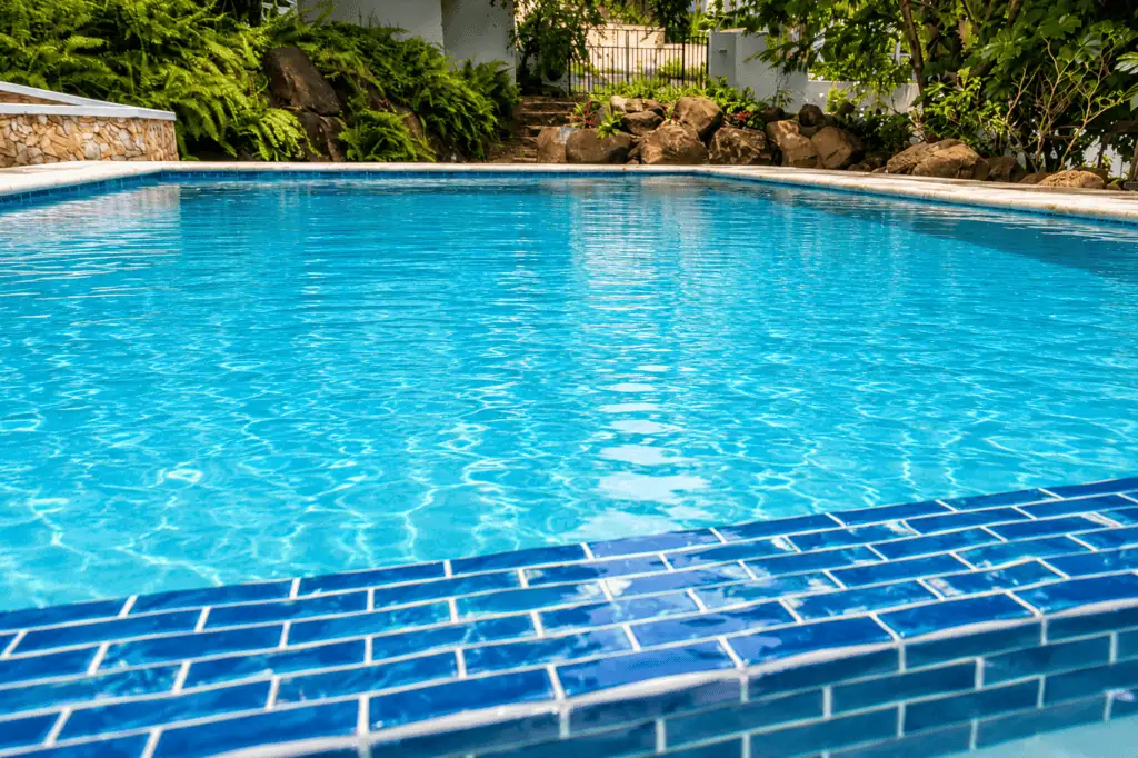 Serene backyard pool with blue tiles and lush greenery.