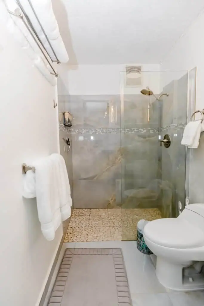 Contemporary bathroom with glass shower, white walls, and beige pebble floor.
