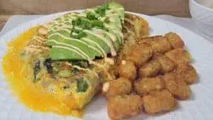 Omelette with avocado slices and fried potato nuggets on a white plate.