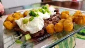 Mofongo with beef, fried plantains, and green onions on a glass plate.
