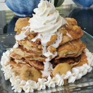 Stack of banana nut pancakes topped with whipped cream and banana slices.