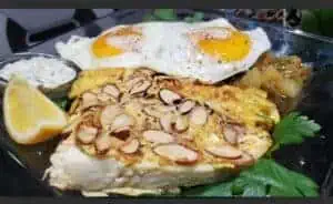 Mexican breakfast with eggs, almond-topped dish, and lemon wedge.