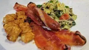 Breakfast plate with bacon, sausage, fried chicken bites, and pasta salad.