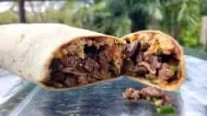 Close-up of a beef burrito with rice, beans, and vegetables inside a flour tortilla.